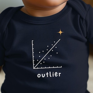 以下が含まれることがあります： 白の散布図のグラフィックと「outlier」の文字がプリントされた、ネイビーブルーのベビーボディスーツ。グラフ線の端には金の星があります。ボディスーツは半袖です。