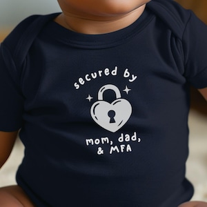 May include: Navy blue baby onesie with the text "secured by mom, dad, & MFA" in white. The design features a white heart-shaped lock with a keyhole and two stars. The onesie is short-sleeved.