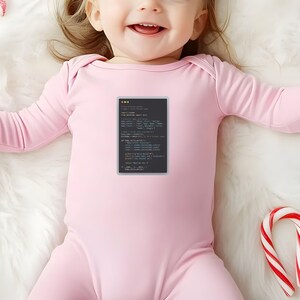 A smiling baby wearing a pink onesie with a programming code printed on it, lying on a white surface with a candy cane nearby.