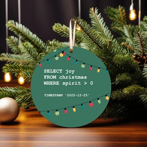 A green circular ornament with a Christmas tree and colorful lights, hanging on a branch.