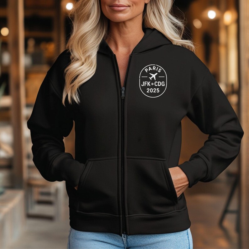 A woman wearing a black hooded jacket with a white logo on the left side of her chest.