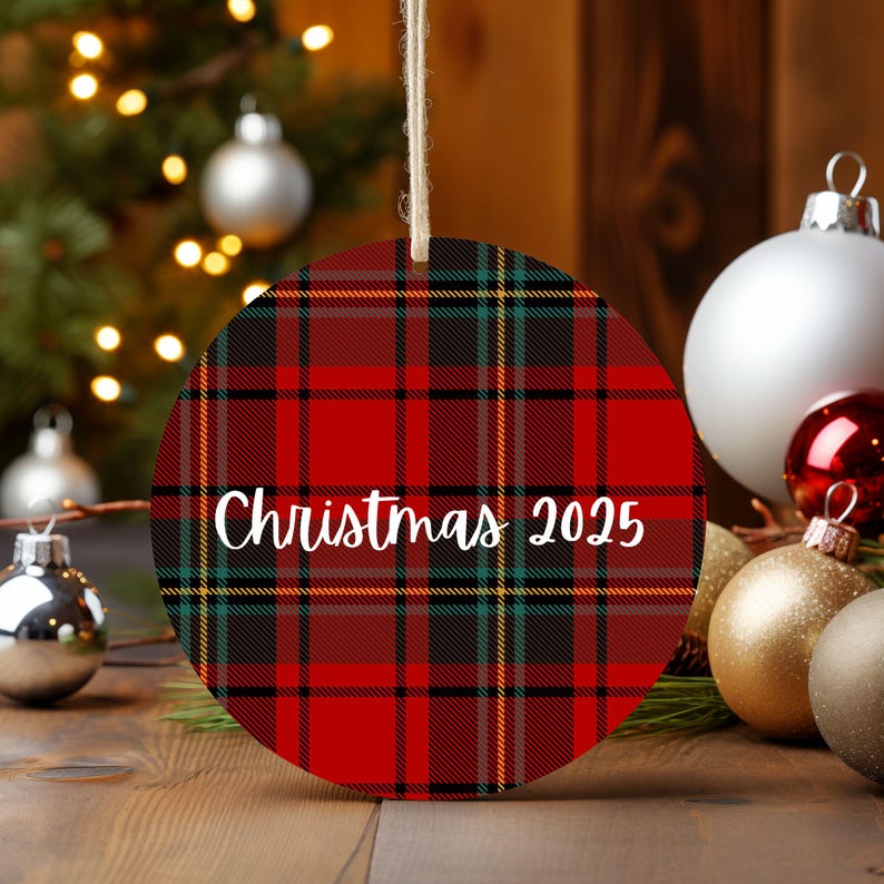 A Christmas ornament with a red and black plaid pattern, hanging on a string, surrounded by other Christmas ornaments and a blurred background of a Christmas tree with twinkling lights.