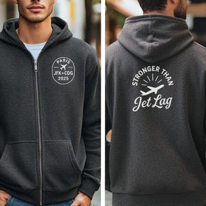 A man wearing a grey hooded sweatshirt with white text and graphics on the back.