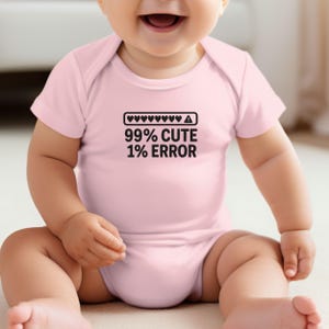 May include: A light pink baby onesie with the text "99% CUTE 1% ERROR" in black. Above the text is a graphic of hearts and an exclamation point. The onesie is short-sleeved and has a snap closure.