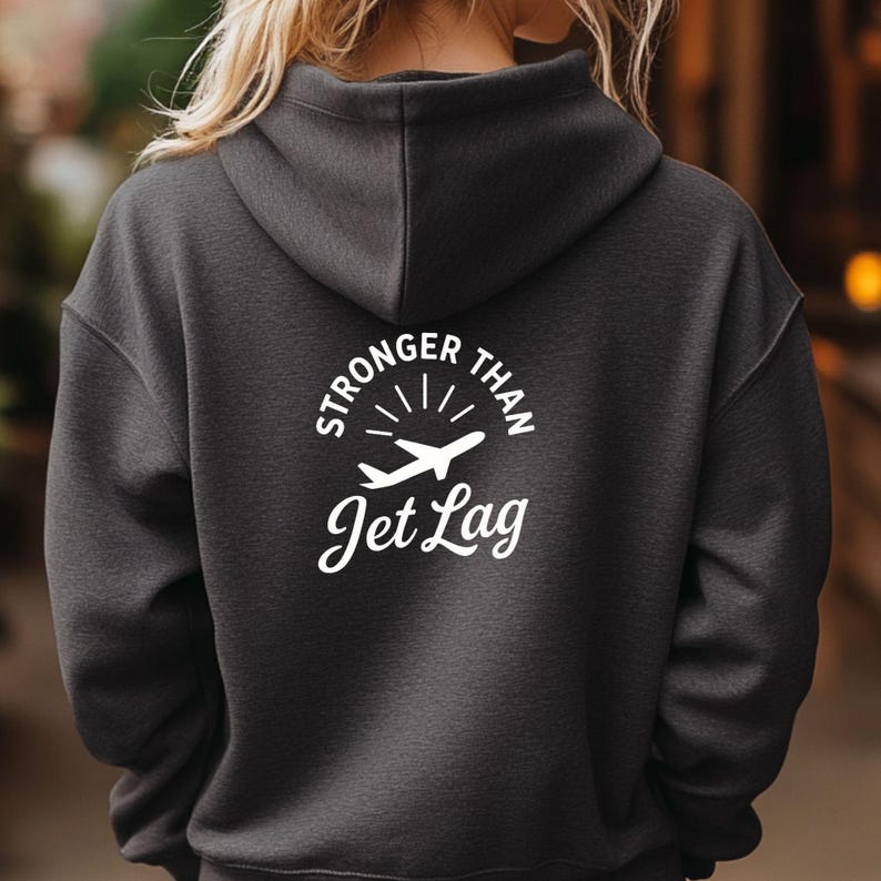 the back of a person wearing a grey hooded sweatshirt with the text "STRONGER THAN Jet Lag" printed on it.