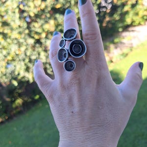 May include: A silver ring with a cluster of round, textured, and slightly raised circles. The ring is worn on a person's finger.