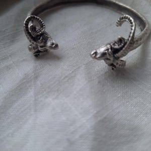 Puede incluir: Pulsera de plata con detalles de cabeza de carnero. La pulsera está abierta y tiene una textura martillada.