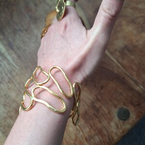 May include: A gold-toned bracelet with a unique, abstract design. The bracelet is made of multiple interconnected loops and curves, giving it a modern and organic look.
