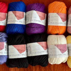 May include: Ten skeins of Loops & Threads Classic Cotton yarn in red, blue, purple, orange, pink, light purple, black, white, and yellow. Each skein features a white label with the text Classic Cotton, 120 yds, 2.5 oz, 109 m, and 70.9 g.