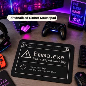 May include: A rectangular black mousepad featuring a white computer error message graphic that reads: Error, Emma.exe has stopped working, Press any key to pretend you're okay. The design includes a warning triangle icon and a loading circle icon.