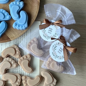 May include: Blue and beige baby foot-shaped soaps in small white organza bags with brown ribbon and a round tag that says "Baby Jeffo 2023".