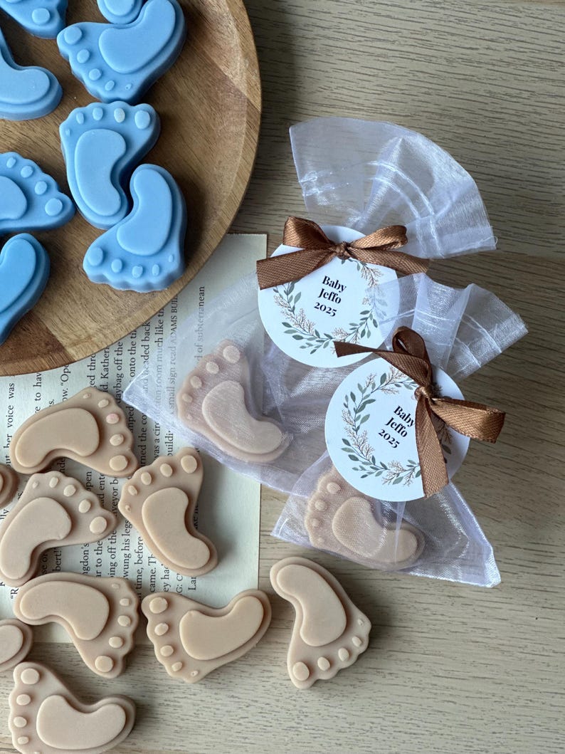 May include: Blue and beige baby foot-shaped soaps in small white organza bags with brown ribbon and a round tag that says "Baby Jeffo 2023".