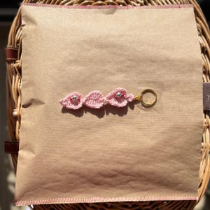 Pode incluir: Chaveiro de folha de croch&ecirc; rosa com contas prateadas e um anel de chave dourado.