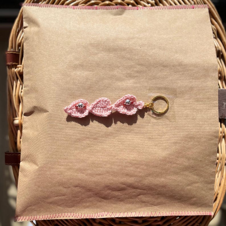 Pode incluir: Chaveiro de folha de croch&ecirc; rosa com contas prateadas e um anel de chave dourado.