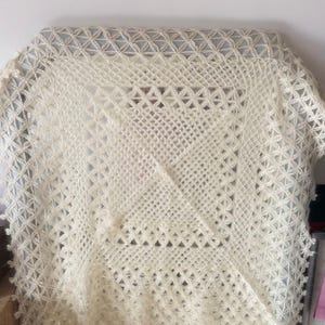 Pode incluir: Um xale branco de croch&ecirc; com um delicado padr&atilde;o de renda. O xale &eacute; feito de fio fino e tem uma sensa&ccedil;&atilde;o macia e arejada.