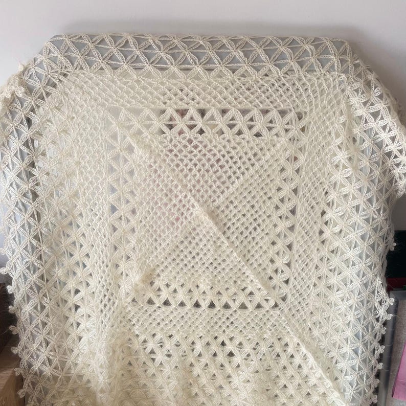 Pode incluir: Um xale branco de croch&ecirc; com um delicado padr&atilde;o de renda. O xale &eacute; feito de fio fino e tem uma sensa&ccedil;&atilde;o macia e arejada.