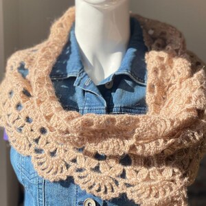 Pode incluir: Uma echarpe de crochê em cor bege claro com um delicado padrão floral. A echarpe é feita de fio macio e tem um design fluido e feminino.
