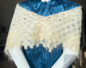Pode incluir: Um xale branco de crochê com um delicado padrão de renda. O xale está drapeado sobre um vestido de cetim azul-turquesa.