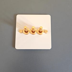 Könnte beinhalten: Eine weiße Lichtschalterplatte mit drei goldenen Kippschaltern.