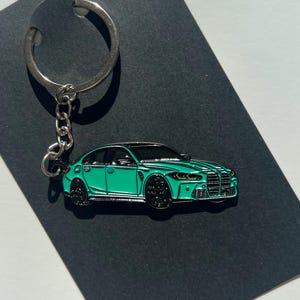 May include: A teal blue car keychain with a silver key ring and chain. The car is a detailed replica of a modern sedan.