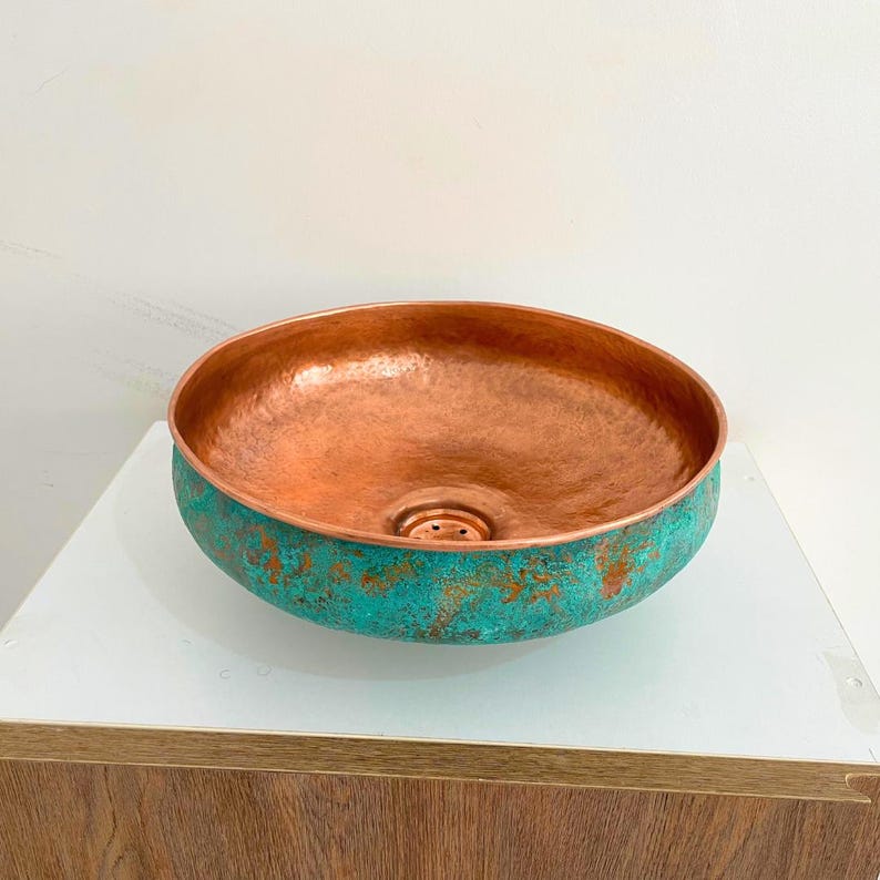 May include: A copper sink with a hammered finish and a turquoise patina. The sink has a round shape and a small drain hole in the center.