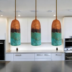 Peut inclure: Trois lampes suspendues en cuivre avec une patine turquoise et brune sont suspendues au plafond d'une cuisine.