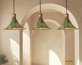 May include: Three pendant lights with a green, textured shade and a gold interior. The lights hang from black cords and have a wooden accent at the top. The text "SHINE BRASS" is visible at the bottom.