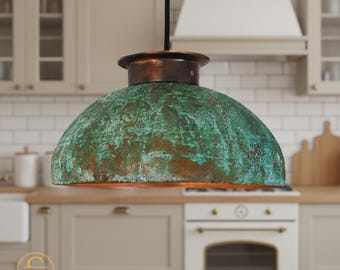 May include: A copper and verdigris pendant light fixture with a dome-shaped shade. The light has a dark cord and is suspended in a kitchen setting. The shade has a textured, aged appearance with shades of green and brown. The fixture is a statement piece.