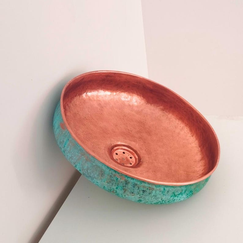 May include: A copper sink with a hammered finish and a green patina. The sink is round and has a drain in the center.