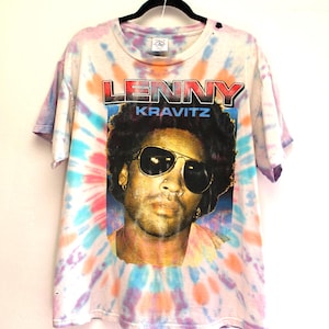 May include: A tie-dye t-shirt with a portrait of Lenny Kravitz wearing sunglasses. The shirt has a colourful spiral pattern in shades of blue, pink, orange, and purple. The name "LENNY KRAVITZ" is printed across the top of the image.