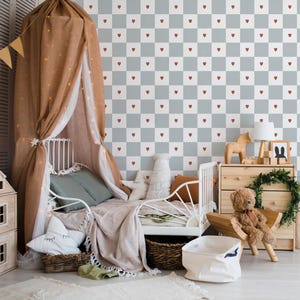Könnte beinhalten: Ein gemütliches Kinderzimmer mit einem weißen Metallbett, einem drapierten Baldachin und einer Tapete mit roten Herzen. Das Zimmer umfasst eine Holzkommode, einen Teddybären und dekorative Kissen.