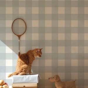 Peut inclure: Un chat roux perché sur des boîtes regarde un chien teckel en peluche. Une raquette de badminton en bois vintage est accrochée à un mur à carreaux bleu et blanc. Un bol de fruits en bois est posé sur une surface en bois.