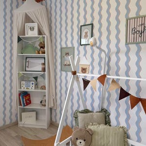 May include: A child's bedroom with blue and white striped wallpaper and a white bed frame. The room features a white bookshelf, a wooden balance board, and framed pictures of bears. Decorative elements include a canopy, pillows, and a banner.