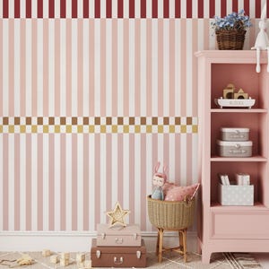 Op de afbeelding: Een roze en witte gestreepte muur met een bruin en gouden geblokte rand. Een roze kast met planken bevat decoratieve items, waaronder een mand met bloemen, een speelgoedkonijn en een stapel koffers. Een stervormig licht staat bovenop de koffers.