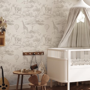 May include: A nursery scene featuring a white crib with a canopy and a small wooden table and chair. The wallpaper has a safari theme with elephants, giraffes, and hot air balloons in a neutral color palette. A wooden guitar and a small shelf with a toy are also visible.