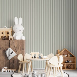 Op de afbeelding: Een kinderspeelkamer met een witte konijnenlamp, houten speelgoed, een kleine tafel en stoelen en een tapijt met een wereldkaartontwerp. De achtergrond heeft gestreept behang en een geschulpte rand.