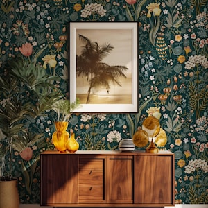Puede incluir: Un papel pintado floral verde oscuro con una foto enmarcada de palmeras cuelga sobre un mueble de madera. El mueble tiene tres cajones y dos puertas. Jarrones y objetos decorativos están encima.