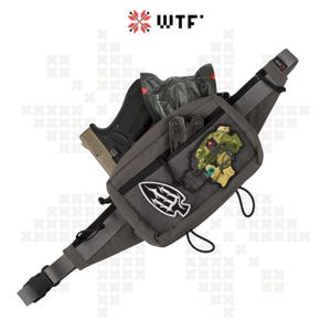 Puede incluir: Una riñonera gris con una correa negra y una hebilla negra. La riñonera tiene varios parches pegados, incluyendo una calavera con un casco, una punta de lanza y una multiherramienta. La riñonera también contiene una pequeña pistola negra y una multiherramienta negra.