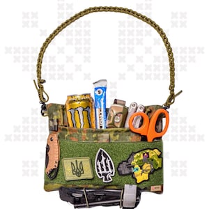 Könnte beinhalten: Eine grüne und braune Tarn-Utility-Tasche mit einem geflochtenen Riemen. Die Tasche ist gefüllt mit verschiedenen Gegenständen, darunter eine Dose Monster-Energy-Drink, ein blauer Energieriegel, eine Taschenlampe, ein Multitool, eine orangefarbene Schere und ein paar Patches. Die Patches beinhalten einen ukrainischen Dreizack, einen stilisierten Dreizack und einen Patch mit einem Soldatenhelm.