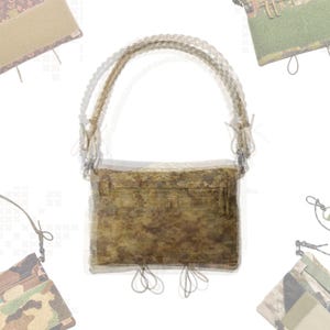May include: A brown and tan camouflage pattern shoulder bag with a braided strap. The bag has a rectangular shape with a flap closure and decorative cord details. The bag is surrounded by other bags with similar camouflage patterns.