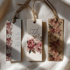 May include: Three floral bookmarks with twine strings. One bookmark has the text "one more page" and a floral border. Another bookmark says "read wildly" with a floral design. The third bookmark has a floral design.