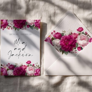 May include: A white wedding invitation and envelope set, adorned with a floral design of pink and white peonies. The invitation reads "Save the Date 15 October 2026" and "Mia and Jackson" in script. Wedding stationery.