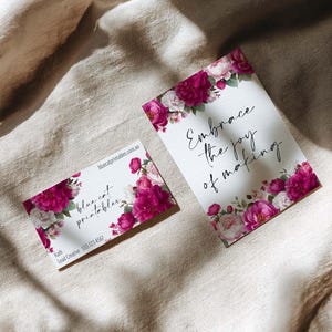 May include: Two white cards with floral designs and text. One card reads "Embrace the joy of making" with a border of pink and white flowers. The other card has the text "blue cat printables" and contact information, also with floral accents.