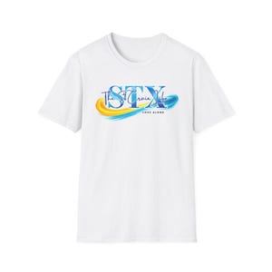 Puede incluir: Camiseta blanca con el texto "STX The St. Croix Life" en escritura azul y amarilla. El diseño incluye una pincelada azul y amarilla. Debajo del texto está la frase "LOVE ALONE".