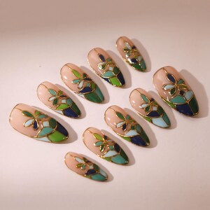 Puede incluir: Conjunto de diez u&ntilde;as postizas con un dise&ntilde;o de vitral. Las u&ntilde;as son de forma almendrada y tienen una base rosa claro con detalles en verde, azul y dorado.