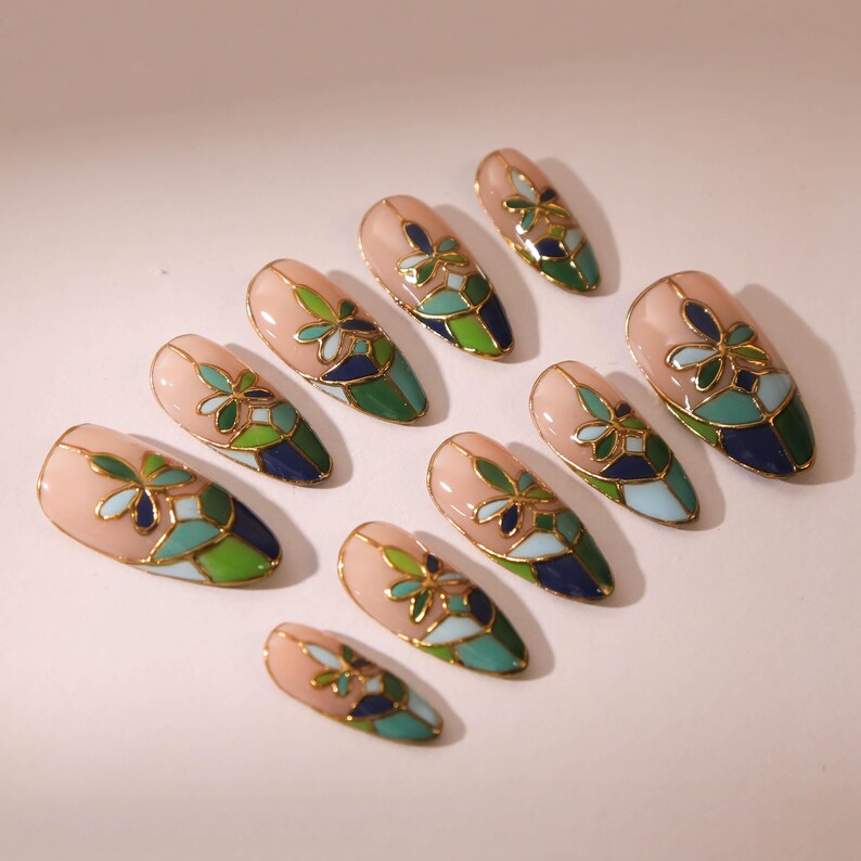 Puede incluir: Conjunto de diez u&ntilde;as postizas con un dise&ntilde;o de vitral. Las u&ntilde;as son de forma almendrada y tienen una base rosa claro con detalles en verde, azul y dorado.