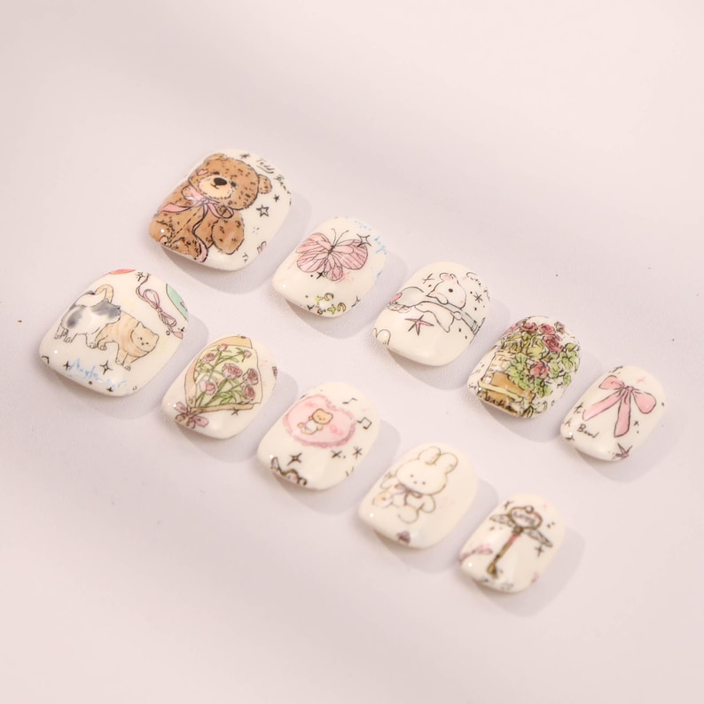 May include: Set of ten white false nails with different cute cartoon designs, including a teddy bear, butterfly, bunny, and flowers.