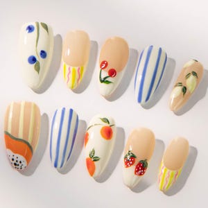 Puede incluir: Diez uñas pintadas con diversos diseños. Los diseños incluyen rayas azules, rayas naranjas y amarillas, cerezas, arándanos, melocotones, fresas y limones. Las uñas son de forma ovalada y están pintadas en blanco, beige y naranja. Una colección de arte de uñas colorida y creativa.