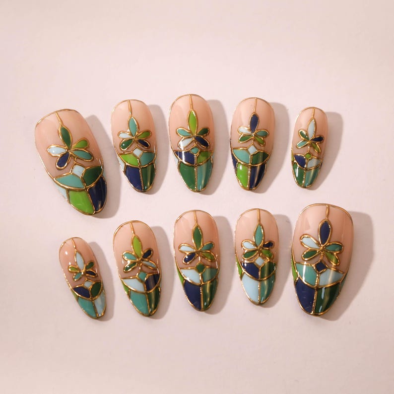 Puede incluir: Conjunto de diez u&ntilde;as postizas con un dise&ntilde;o de vitral. Las u&ntilde;as son de forma ovalada y presentan un patr&oacute;n floral en tonos verdes, azules y dorados.