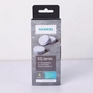 Könnte beinhalten: Eine Schachtel mit Siemens EQ.series 2-in-1 Reinigungstabletten für Kaffeevollautomaten. Die Schachtel ist grau mit weißem Text und einem schwarzen Aufhänger. Drei runde, hellblaue Tabletten sind sichtbar.